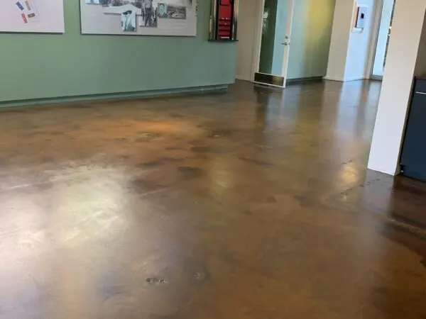 A room with green walls and polished concrete floors. The walls have framed pictures, and there are doors in the background.