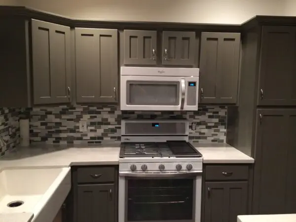 Modern kitchen with grey cabinets, white countertops, and a tile backsplash. Features include a built-in microwave, gas stove, and a white sink.